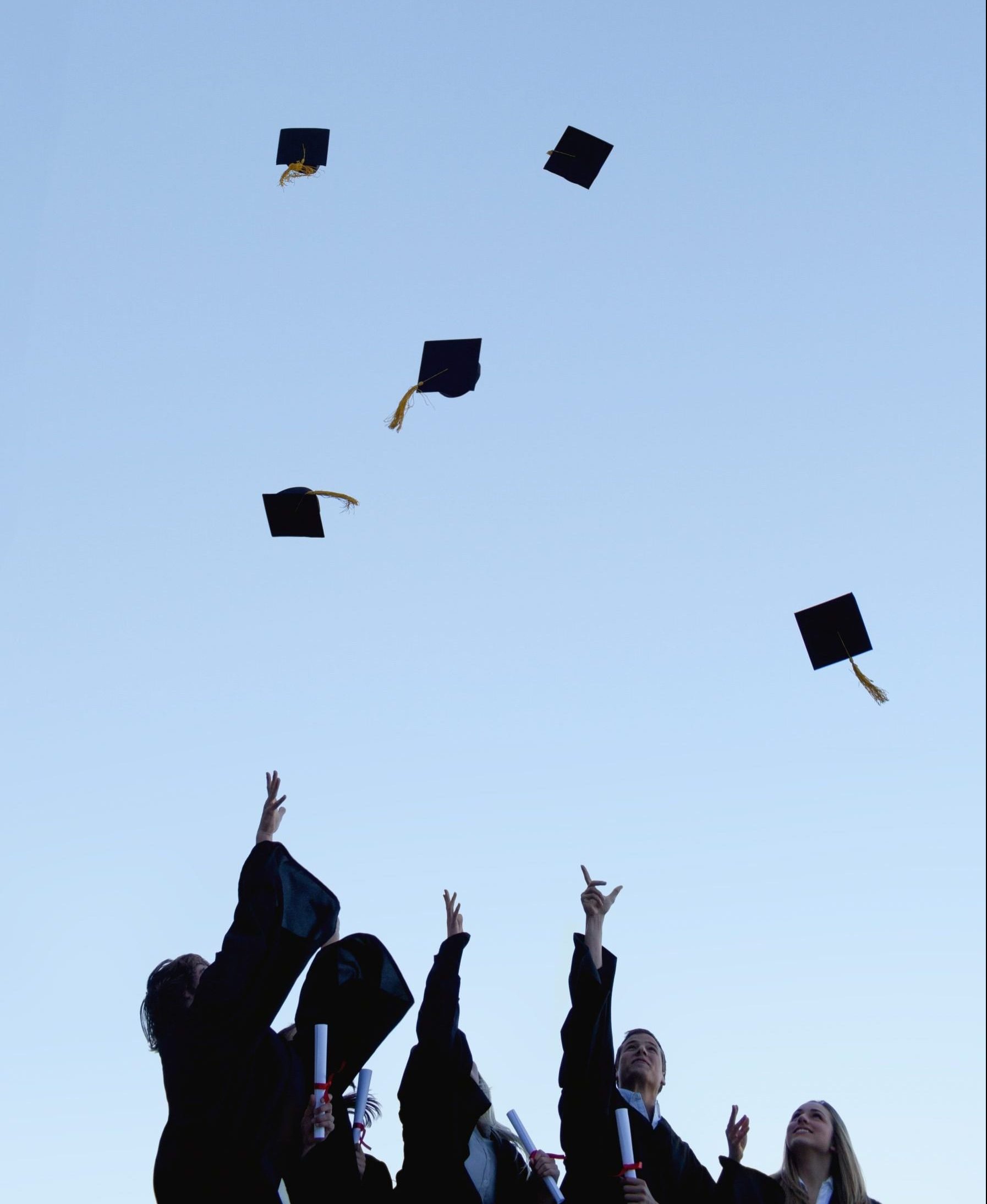 Low angle-shot of five grad students throwing their hats high in the sky
